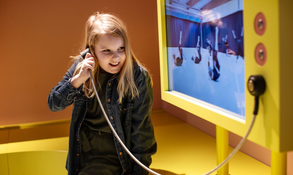 Lapsi kuuntelee museossa videoruudun ääntä kädessä pidettävästä luurista.