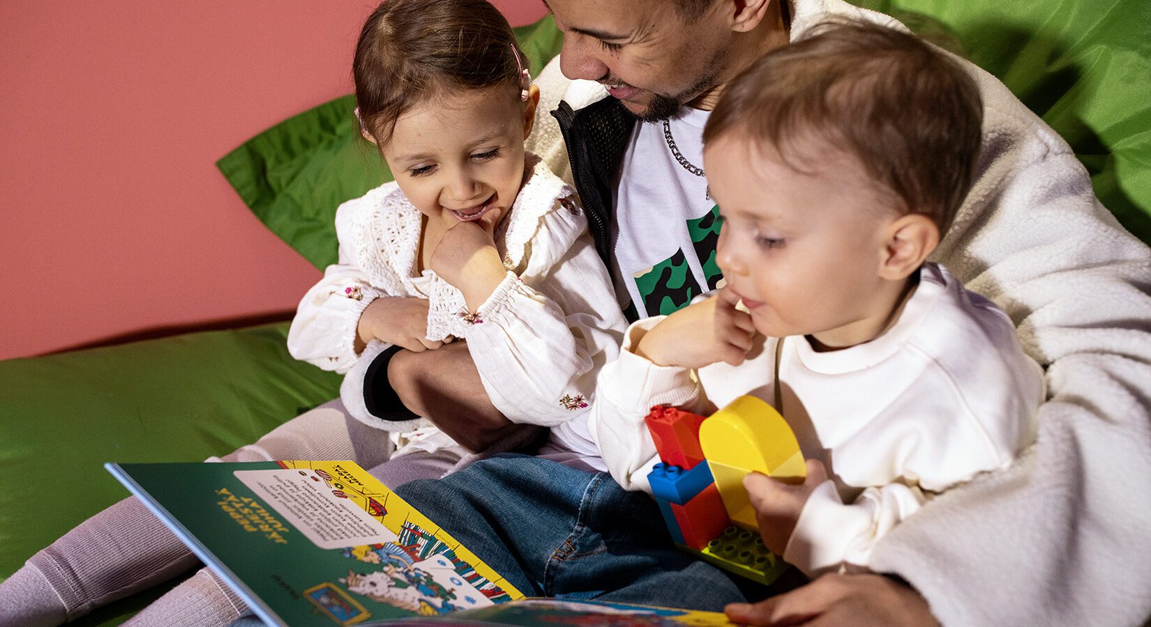 Aikuinen ja kaksi pientä lasta tutkivat yhdessä kuvakirjaa
