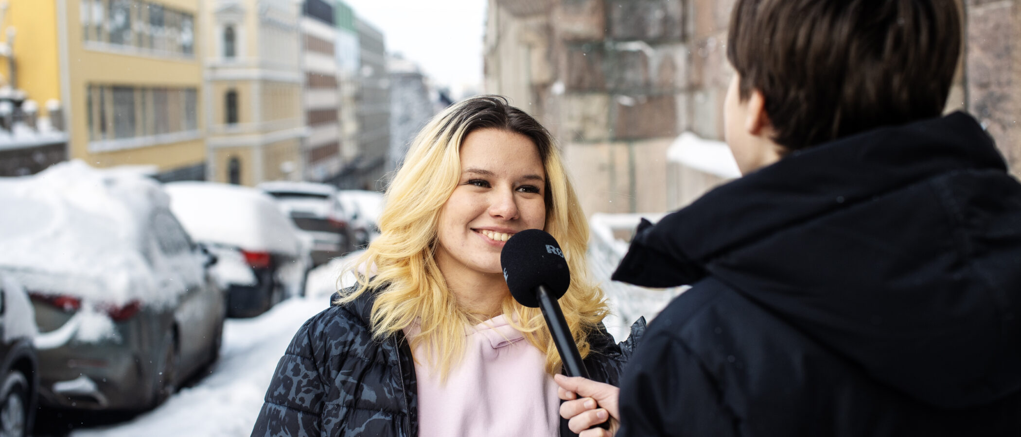 Toinen nuori pitää mikrofonia ja toinen puhuu siihen: haastattelutilanne ulkona kadulla.